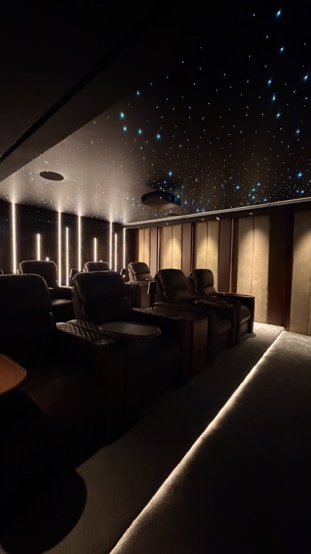 Reclining cinema seats beneath a star ceiling, with illuminated aisles and wall lighting.