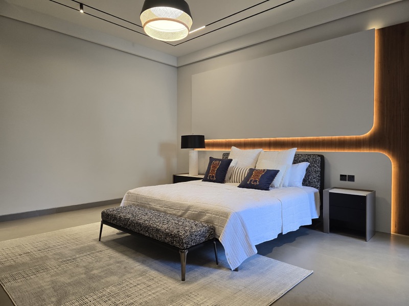 A bedroom with pendant lighting, ceiling tracks and warm lighting around the headboard.