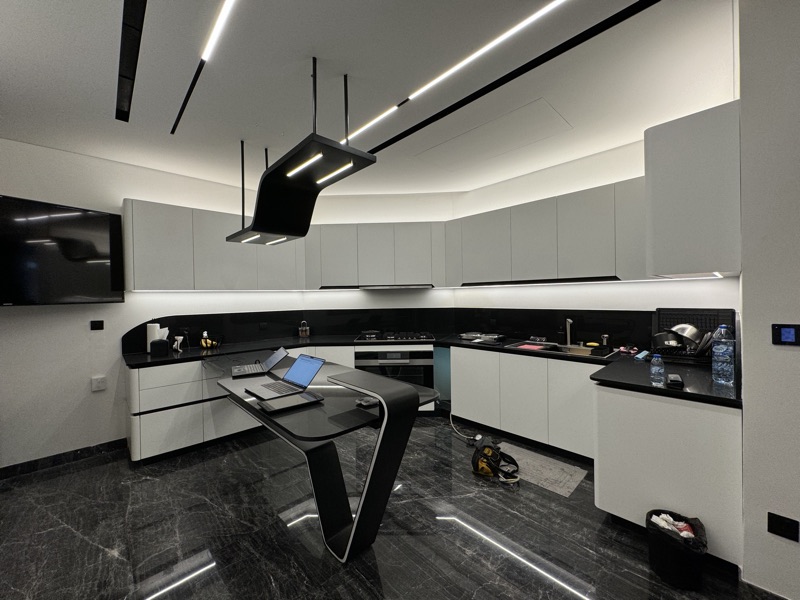 A kitchen with linear and pendant lighting, a wall-mounted screen and installation equipment visible.