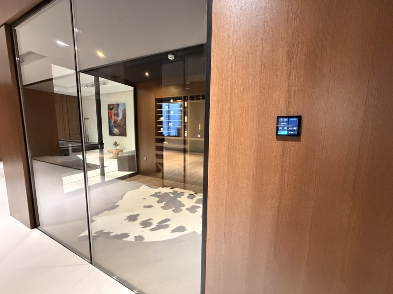 A compact room-control touchscreen installed on a timber wall.